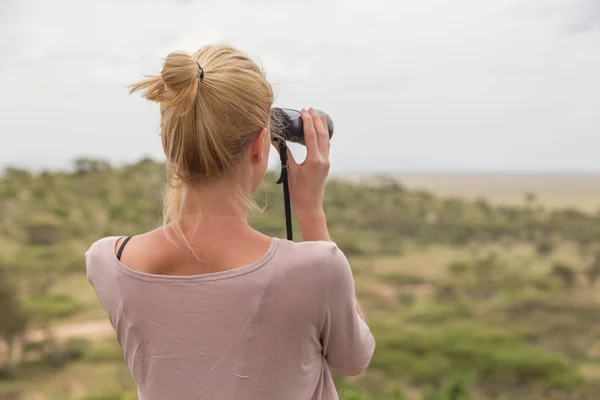 Turista feminina olhando através de binóculos em safári Africano no parque nacional Serengeti. Tanzânia, África . — Fotografia de Stock