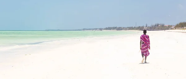 Maasai warrior walking on picture perfect tropical sandy beach. Paje, Zanzibar, Tanzania. — Stock Photo, Image