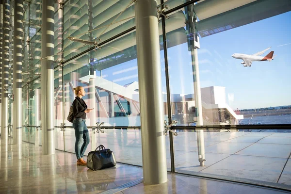 Giovane donna in attesa in aeroporto, guardando attraverso la finestra del cancello . — Foto Stock