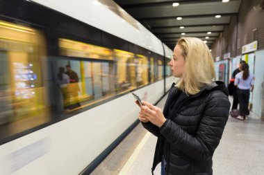 Kadın metro için bekleyen bir cep telefonu ile.