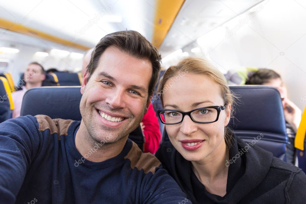 Young handsome couple taking a selfie on commercial airplane.