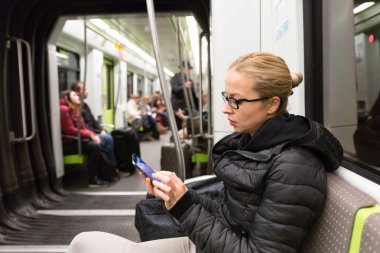 Metrodaki cep telefonu ekranından okuyan genç bir kız..