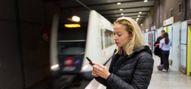 Kadın metro için bekleyen bir cep telefonu ile.