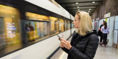 Kadın metro için bekleyen bir cep telefonu ile.