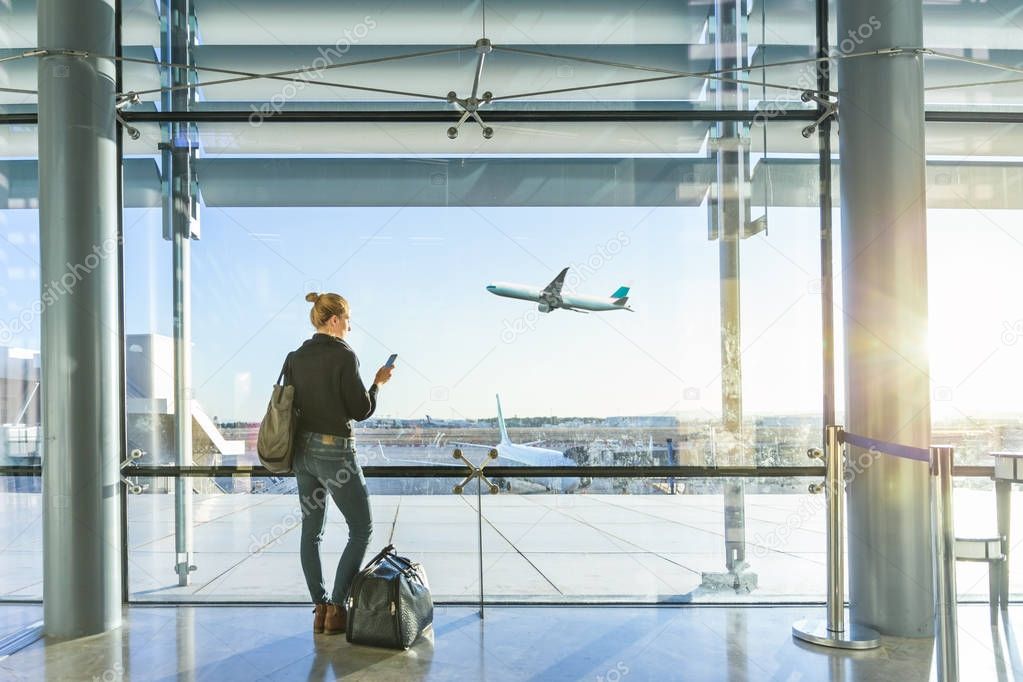 Young woman waiting at airport, looking through the gate window.