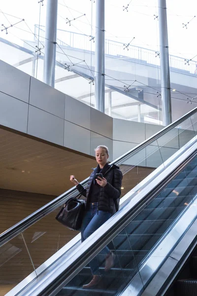 Mujer de negocios con gran bolsa negra y teléfono móvil descendiendo en escaleras mecánicas . —  Fotos de Stock