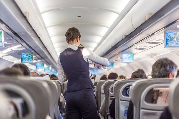 Interior of commercial airplane with stewardess serving passengers on seats during flight. — Stock Photo, Image