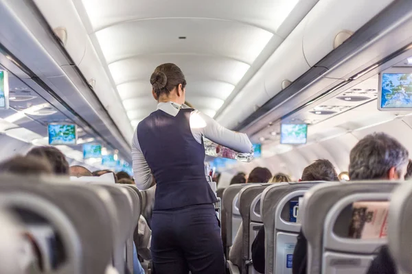 Interiör i kommersiella flygplan med flygvärdinna som betjänar passagerare på sittplatser under flygning. — Stockfoto