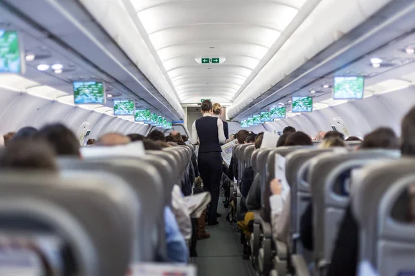 Interior do avião comercial com hospedeira servindo passageiros em assentos durante o voo . — Fotografia de Stock