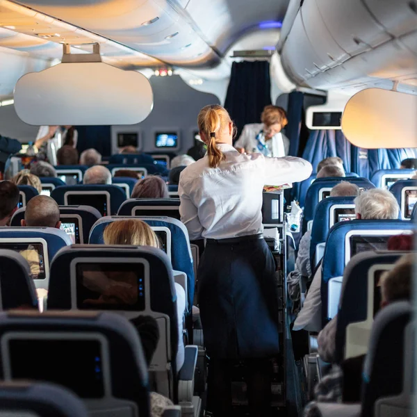 Innenraum eines großen Verkehrsflugzeugs mit Stewardessen, die Passagiere während des Fluges auf den Sitzen bedienen. — Stockfoto