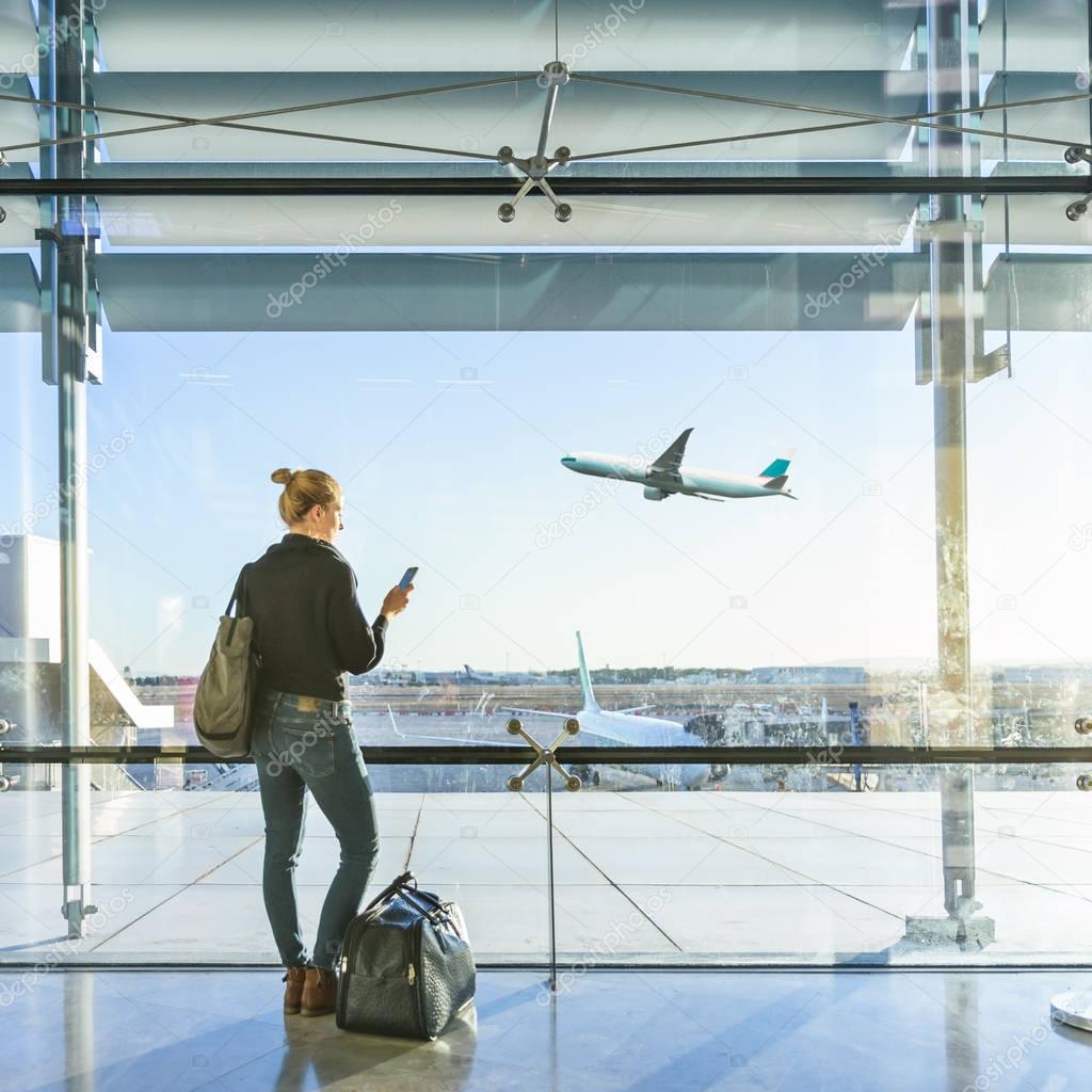 Young woman waiting at airport, looking through the gate window.