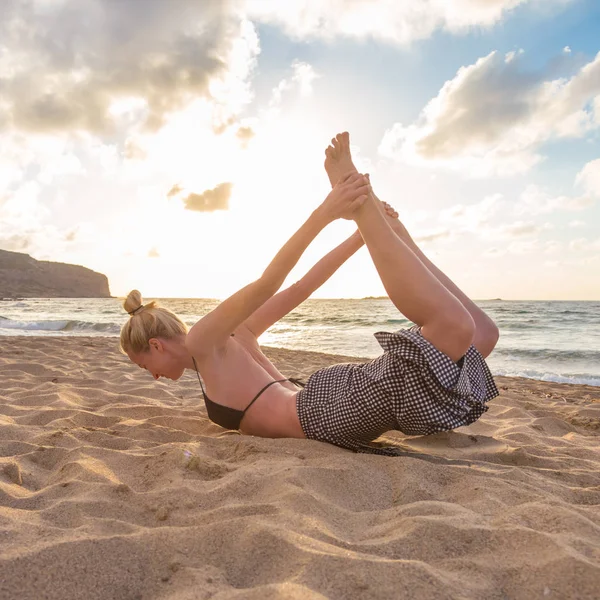 Žena cvičí jógu na mořské pláži při západu slunce. — Stock fotografie