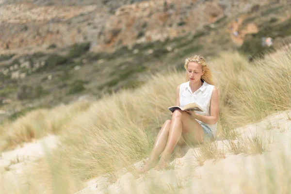 Mujer leyendo libro, disfrutando del sol en la playa . — Foto de Stock