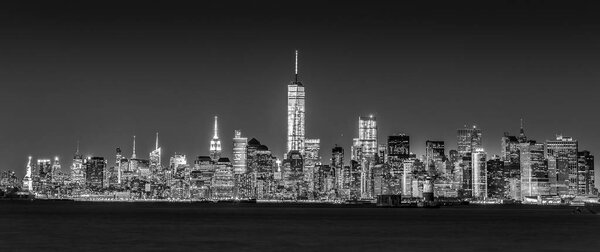 New York City Manhattan downtown skyline at dusk with skyscrapers illuminated over Hudson River panorama. Horizontal composition, black and white image.