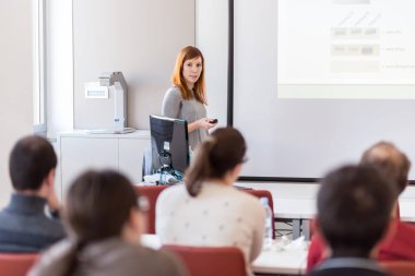 Üniversitedeki konferans salonunda sunum yapan kadın..