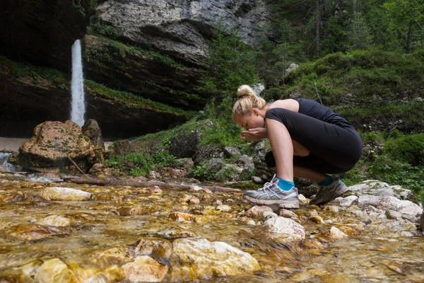 Actieve sportieve vrouw drinkwater uit buiten stream met haar handen. — Stockfoto