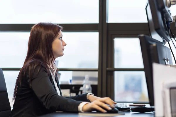 Casual businesswoman working in office, sitting at desk, typing on keyboard, looking at computer screen.