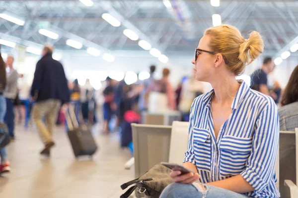 Frau benutzt ihr Handy, während sie am Abflugsteig des internationalen Flughafens auf ein Flugzeug wartet. — Stockfoto