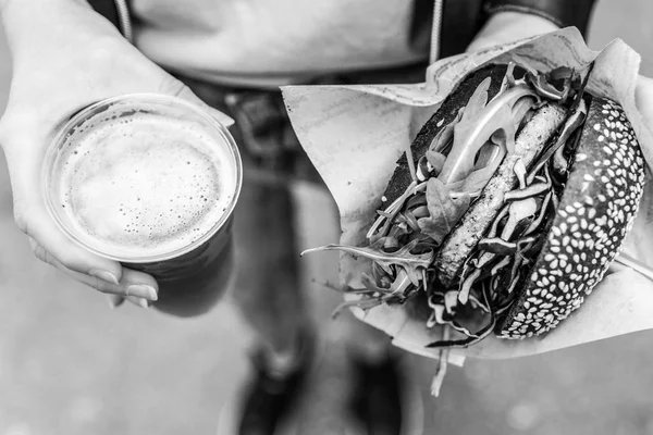 Mãos femininas segurando delicioso salmão orgânico hambúrguer vegetariano e cerveja IPA caseira . — Fotografia de Stock