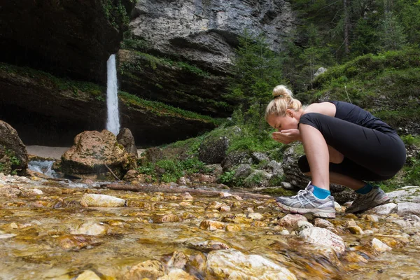 Active sporty woman drinking water from outdoor stream with her hands. — Stock Photo, Image