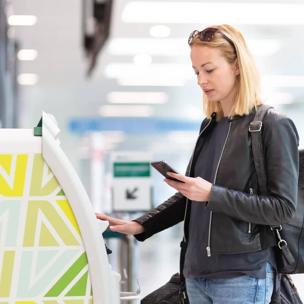 Havaalanında biniş kartı almak akıllı telefon uygulama ve check-in makinesini kullanarak rahat Kafkas kadın.