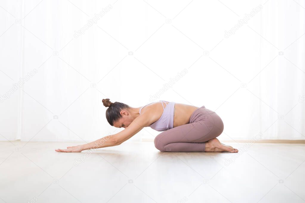 Portrait of gorgeous active sporty young woman practicing yoga in studio. Beautiful girl practice Ardha Kurmasana, half tortoise yoga pose. Healthy active lifestyle, working out indoors in gym