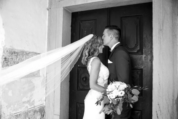 El beso. Novio besos novia en la frente delante de la iglesia portal . — Foto de Stock
