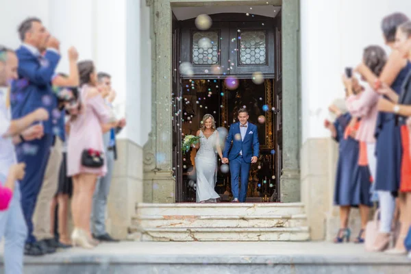 Gli sposi che escono dalla chiesa dopo la cerimonia nuziale, la famiglia e gli amici che celebrano il loro amore con la doccia di bolle di sapone, personalizzato minando bagno di riso tradizionale — Foto Stock