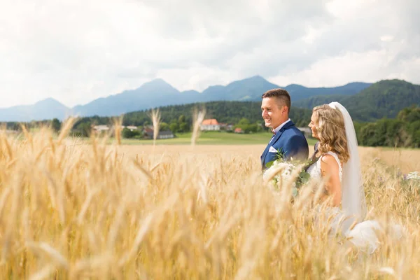 Νύφη αγκαλιάζει τον γαμπρό τρυφερά σε χωράφι με σιτάρι κάπου στη σλοβενική ύπαιθρο. — Φωτογραφία Αρχείου
