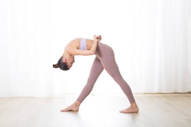 Portrait of gorgeous active sporty young woman practicing yoga in studio. Beautiful girl practice Dandayamana Bibhaktapada Jauushirasana, standing separate leg head to knee pose