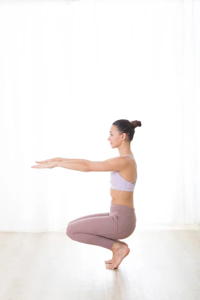 Portrait of gorgeous active sporty young woman practicing yoga in studio. Beautiful girl practice Utkatasana, awkward yoga pose. Healthy active lifestyle, working out in gym — Zdjęcie stockowe