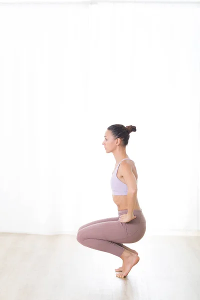 Portrait of gorgeous active sporty young woman practicing yoga in studio. Beautiful girl practice Utkatasana, awkward yoga pose. Healthy active lifestyle, working out in gym — Zdjęcie stockowe