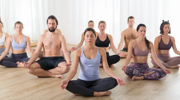 Grupo de jovens desportivos pessoas atraentes no estúdio de ioga, praticar aula de ioga com instrutor, sentado no chão em Siddhasana, fácil postura de ioga sentado. Estilo de vida ativo saudável, exercitando-se no ginásio — Fotografia de Stock