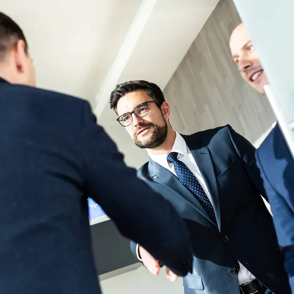 Bir grup kendine güvenen iş adamı modern ofislerdeki iş görüşmelerinde tokalaşarak selamlaşıyor ya da el sıkışarak anlaşmayı bitiriyor.. — Stok fotoğraf