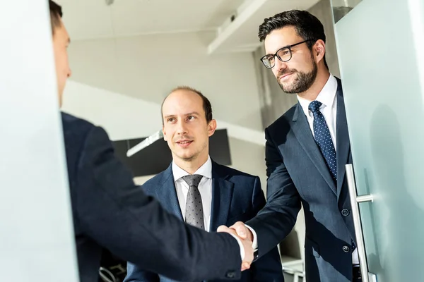 Gruppe selbstbewusster Geschäftsleute, die sich bei einem Geschäftstreffen im modernen Büro per Handschlag begrüßen oder die Vereinbarung durch Händeschütteln abschließen. — Stockfoto