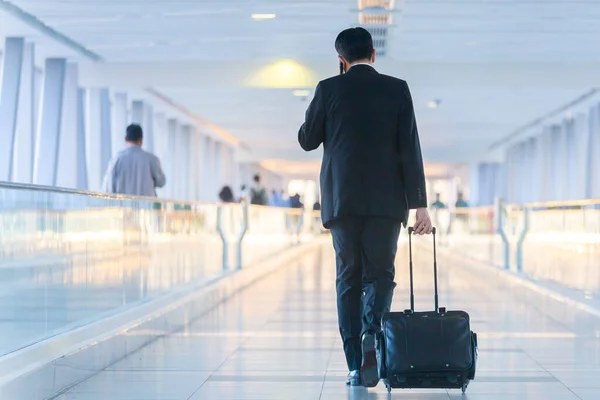 Uomo d'affari che cammina e porta una valigia del carrello all'ingresso, parlando con un cellulare. Business travel concept . — Foto Stock