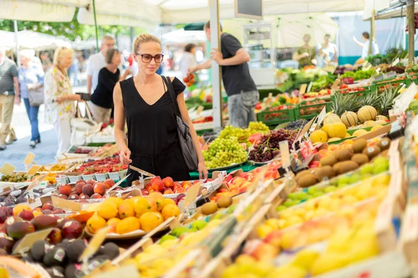 Kadın yerel gıda pazarından meyve ve sebze alıyor. Çeşitli organik sebzelerle market tezgahı — Stok fotoğraf