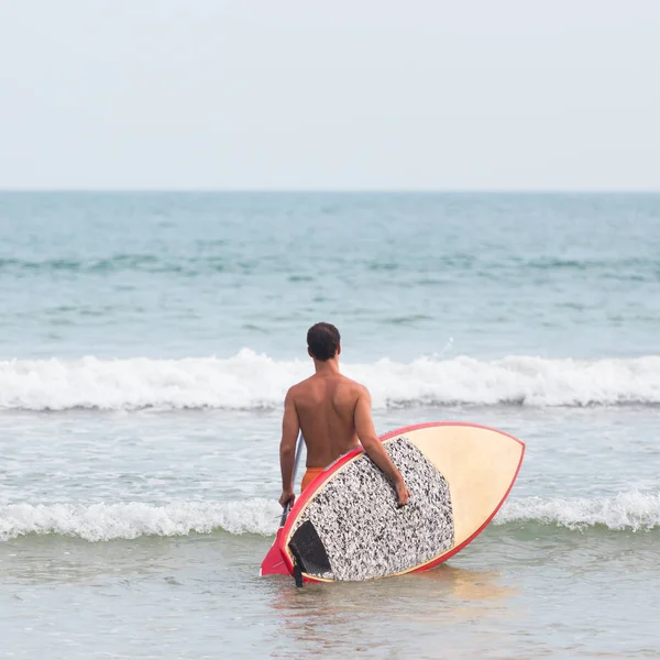 Widok z tyłu nierozpoznawalny mężczyzna surfer na tropikalnej plaży z deski surfingowej supsup i wiosła w jego rękach — Zdjęcie stockowe