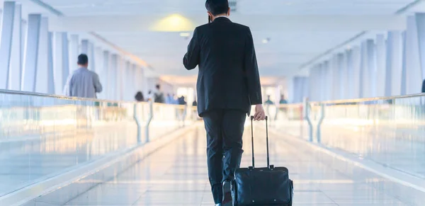 Homme d'affaires marchant et roulant une valise de chariot dans le hall, parlant sur un téléphone portable. Concept de voyage d'affaires . — Photo