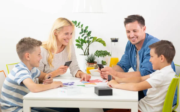 Ευτυχισμένος νέος οικογένεια παίζοντας παιχνίδια με χαρτιά στο τραπέζι του σύγχρονου σπιτιού φωτεινό. — Φωτογραφία Αρχείου