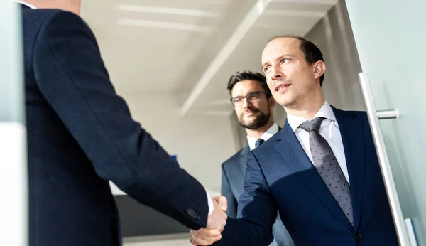 Skupina sebevědomých podnikatelů, kteří si potřásají rukou na obchodní schůzce v moderní kanceláři nebo uzavírají dohodu potřesením rukou. — Stock fotografie