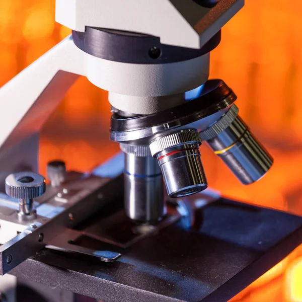 Primer plano de las lentes del microscopio centradas en una muestra con luz naranja cálida . — Foto de Stock