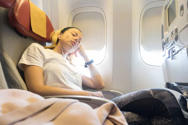 Tired blonde casual caucasian lady napping on uncomfortable seat while traveling by airplane. — Stock Photo, Image