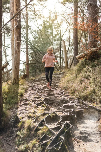 Aktiv sportig kvinna lyssnar på musiken när hon springer i höstskogen. Kvinnliga löpare utbildning utomhus. Friska livsstil bild av unga kaukasiska kvinna jogga utanför — Stockfoto