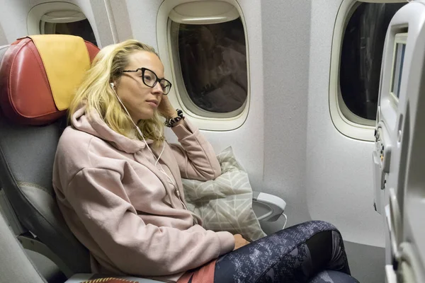 Tired blonde casual caucasian lady napping on uncomfortable seat while traveling by airplane. Commercial transportation by planes. — Stock Photo, Image
