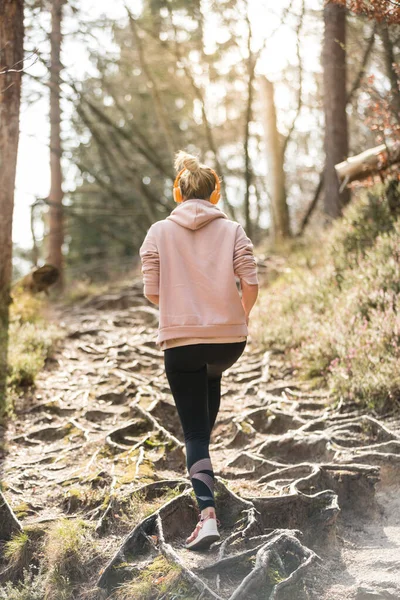 Rear view of active sporty woman listening to the music while running in autumn fall forest. Female runner training outdoor. Healthy lifestyle image of young caucasian woman jogging outside — Stock Photo, Image