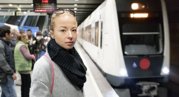 Kışlık montlu genç bir kadın işe gidiyor, tren istasyonunun peronunda treninin gelmesini bekliyor. Toplu taşıma — Stok fotoğraf
