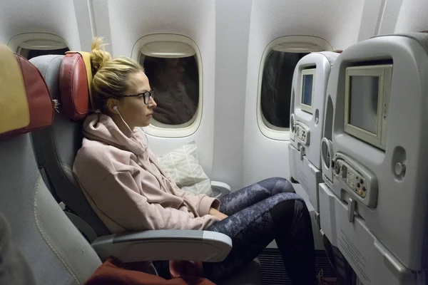 Спортивна випадкова молода блондинка біла жінка дивиться фільм під час подорожі літаком біля вікна. Комерційні перевезення літаками — стокове фото