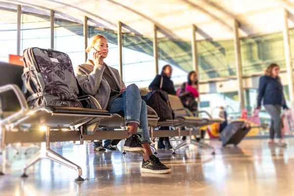 Mujer joven rubia casual usando su teléfono celular mientras espera para abordar un avión en las puertas de salida del aeropuerto . —  Fotos de Stock