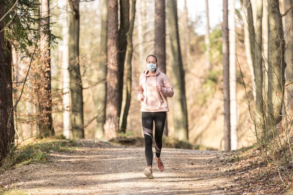 O vírus Corona, ou Covid-19, está se espalhando por todo o mundo. Retrato de mulher esportiva caucasiana usando uma máscara facial de proteção médica enquanto corre na natureza . — Fotografia de Stock